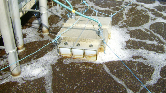 Ett mätinstrument med slangar ligger i vatten på en avloppsanläggning, hålls fast med snören.