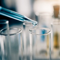 Cylinder sample tubes lined up in a chemical lab and a  pipette dropping in blue liquid into one of the tubes. 