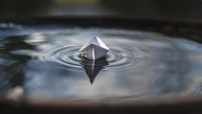 En båt, vikt av papper, som flyter på en vattenyta.