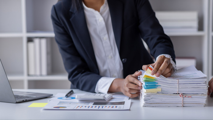 Business Employee Asian woman hand working in Stacks paper files for searching and check unfinished document archives on folders papers at busy work desk workplace office. Business Documents concept.