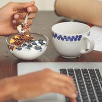 En person äter frukost vid sin dator
