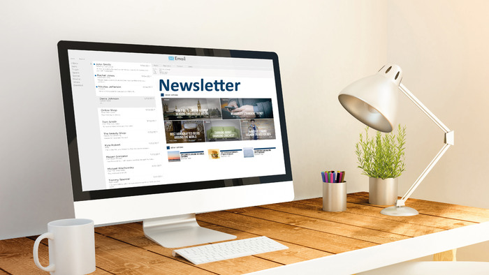 A computer stands on a desk. A newsletter can be seen on the computer screen.