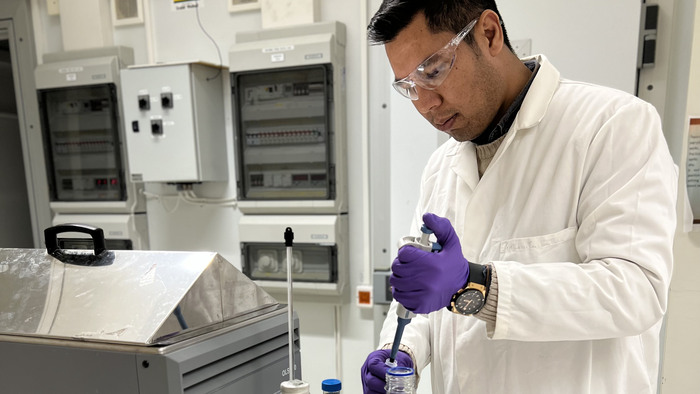 En mörkhyad man med mörkt hår och  vit rock arbetar i ett laboratorium.