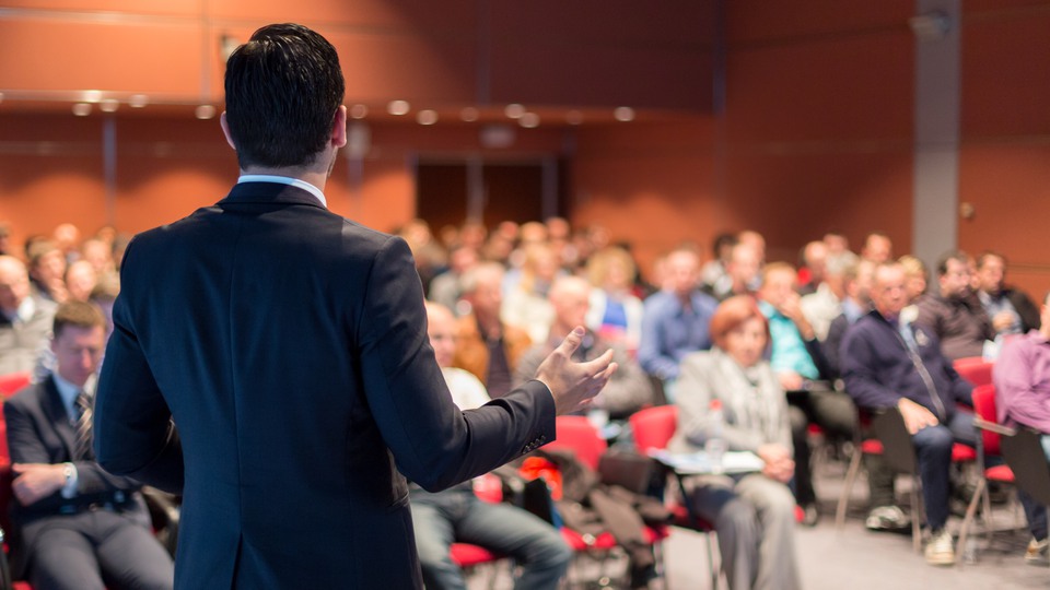 Speaker giving a talk on corporate business conference. Unrecognizable people in audience at conference hall. Business and Entrepreneurship event.