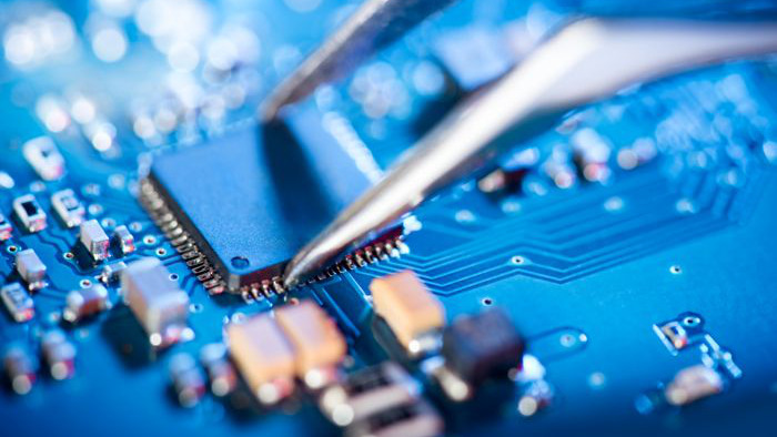 Electronic technician holding tweezers and assemblin a circuit board.